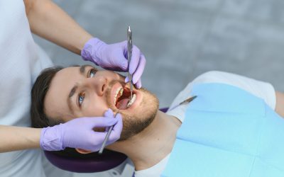 young bearded man sitting in dental chair, visiting modern dental clinic, having regular checkup, woman dentist