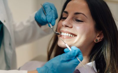 Dentist wearing blue gloves examining teeth of smiling young woman during a thorough dental checkup in a bright, clean clinic, ensuring optimal oral health and hygiene